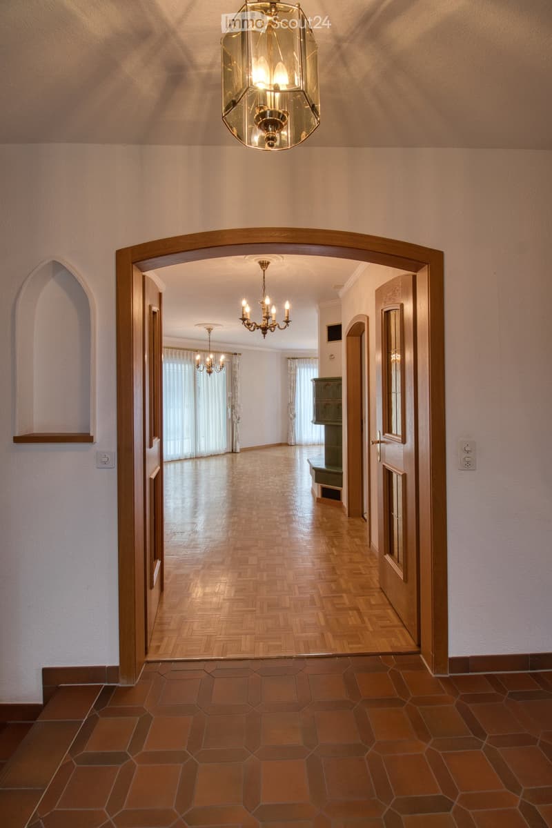Wooden double doors, tiled floor, wood parquet floor, white walls, ceiling with chandeliers, arched doorway