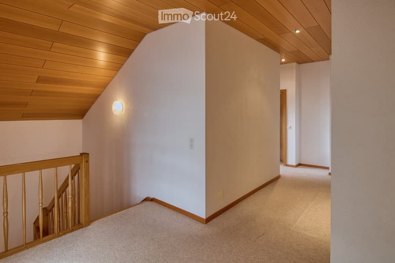 Empty room with wooden ceiling, white walls, beige flooring, and wooden railing.