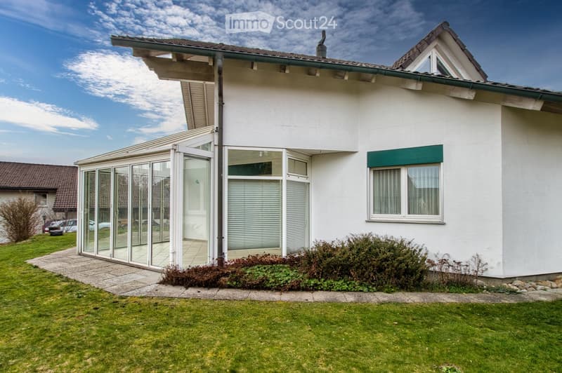 Detached house, white exterior, glass windows, glass door, balcony, shrubs, lawn, and a house in the background