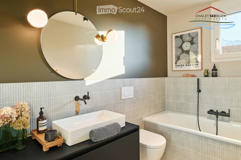 White tiles, large mirror, modern sink, bathtub, white toilet, flowers, wall-mounted lights
