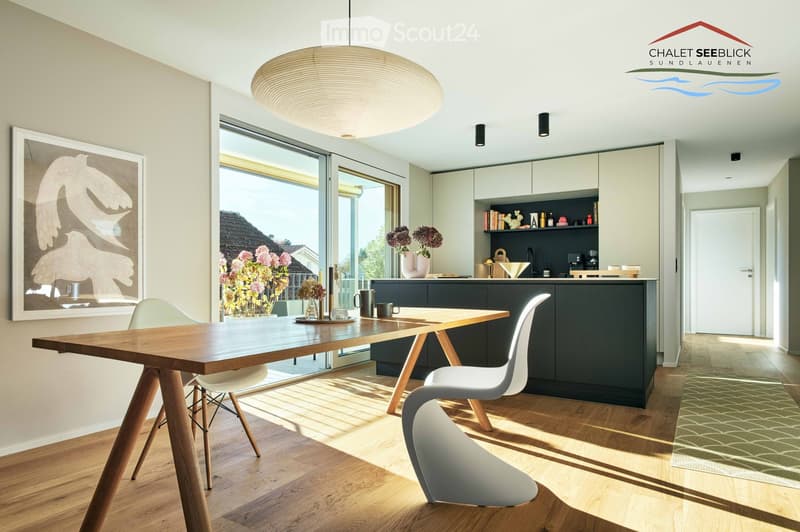 Wooden dining table, glass door leading to a balcony, modern open kitchen, wooden floor