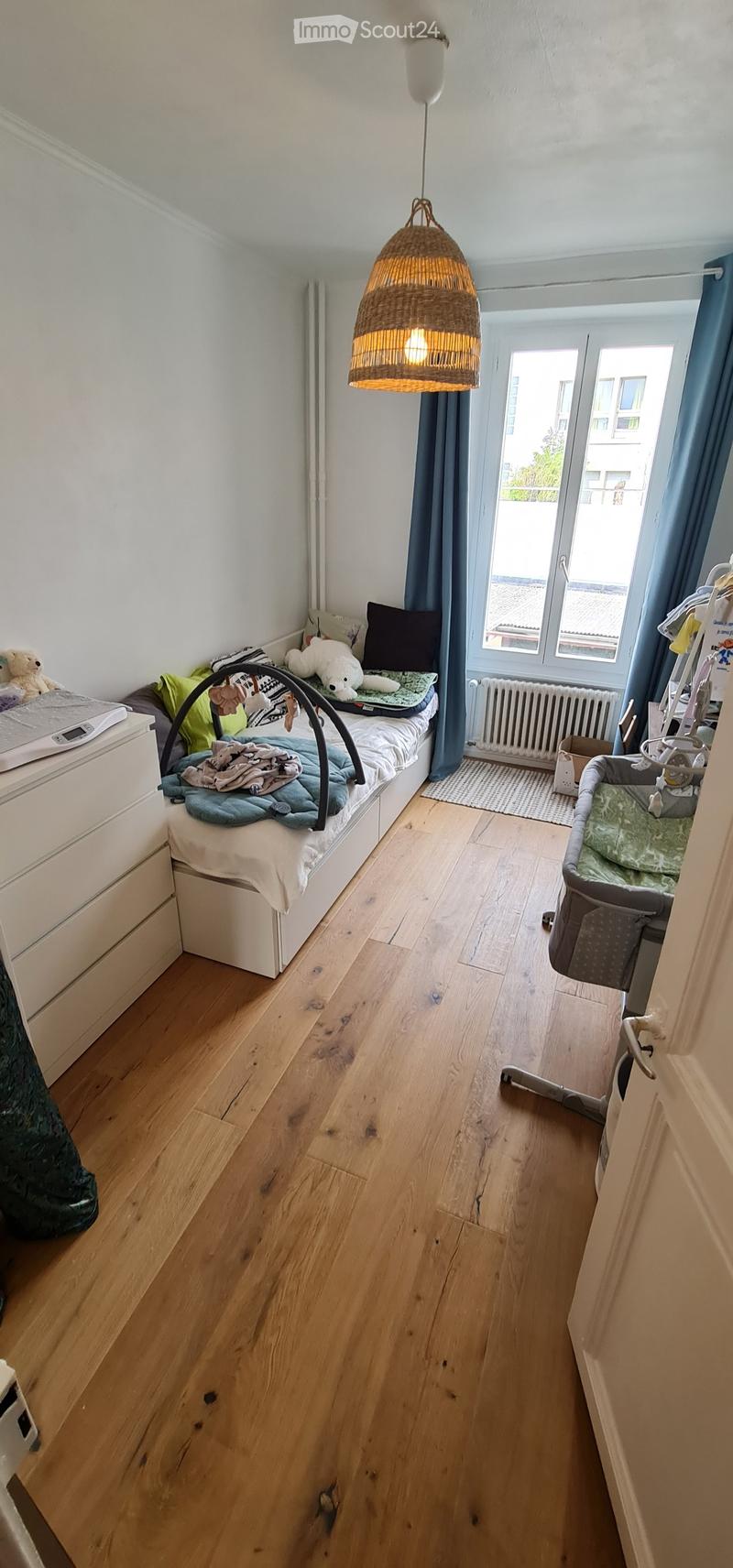 bedroom with bed, bedside table, lamp, drawers, baby bed, radiator, window with curtain