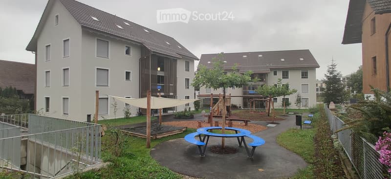 Pathway in courtyard, play area, benches, trees, houses in background