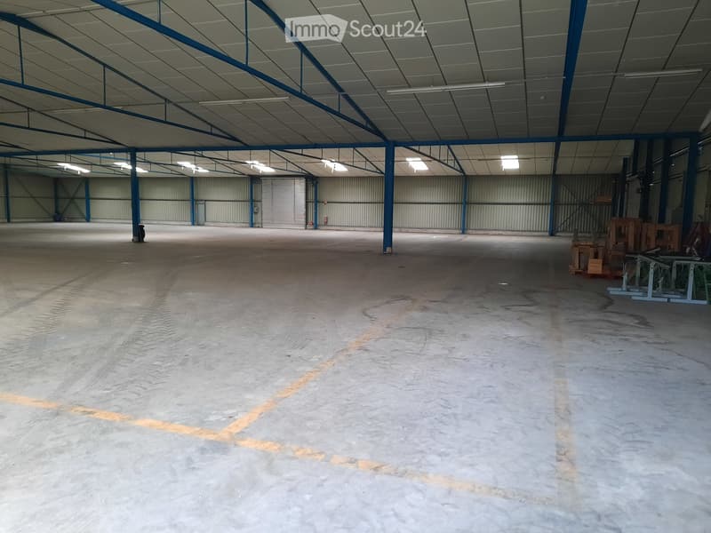 large open space with high ceilings, concrete floor, metal beams, multiple roller doors, and some office equipment