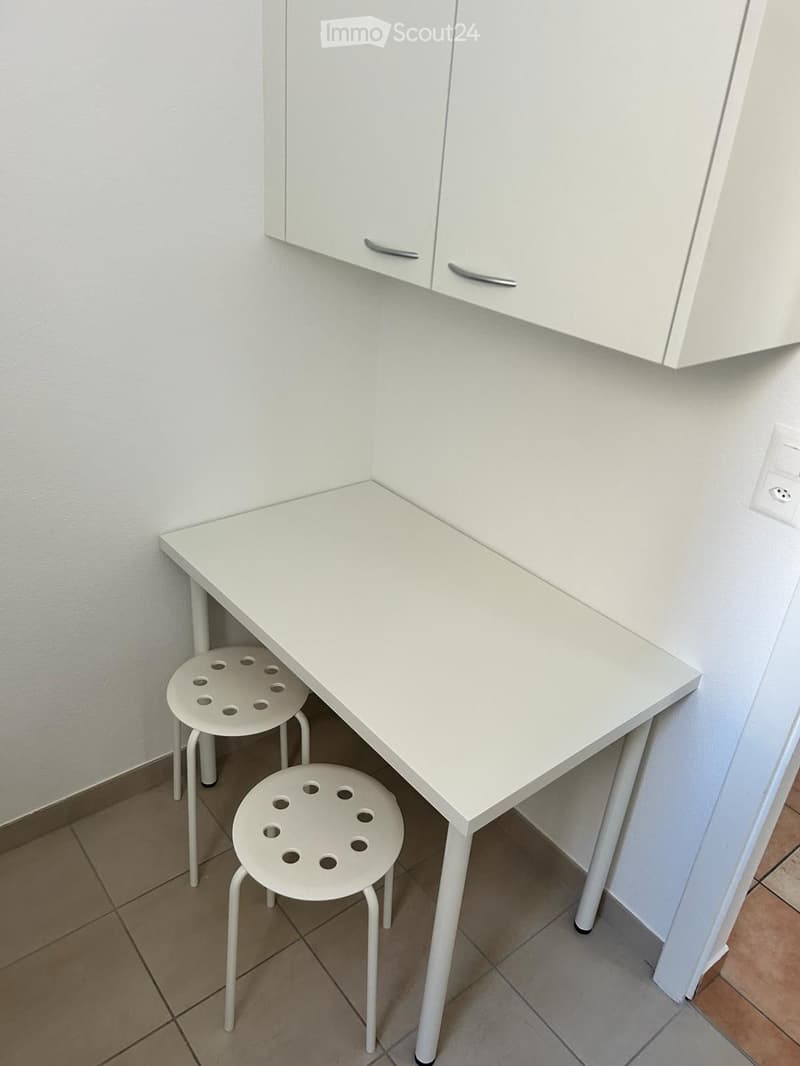 white desk with 2 stools, white wall, cabinets mounted on the wall, tiled floor