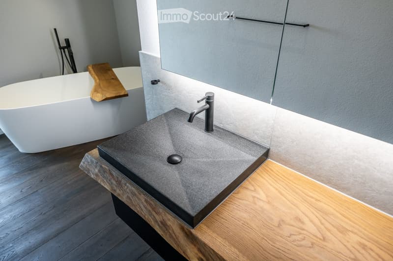 modern bathroom, white bathtub, wooden towel holder, black and grey sink with faucet