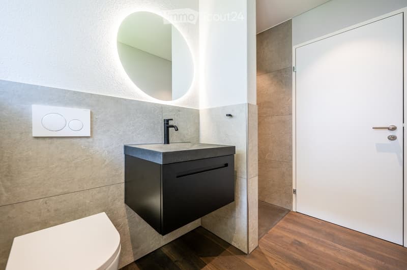 small bathroom with toilet, countertop, sink, faucet, round mirror, and wooden floor