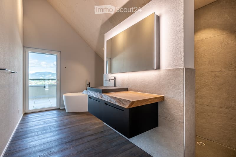 modern bathroom with large mirror, wooden countertop, white bathtub, glass door to balcony, sloped ceiling