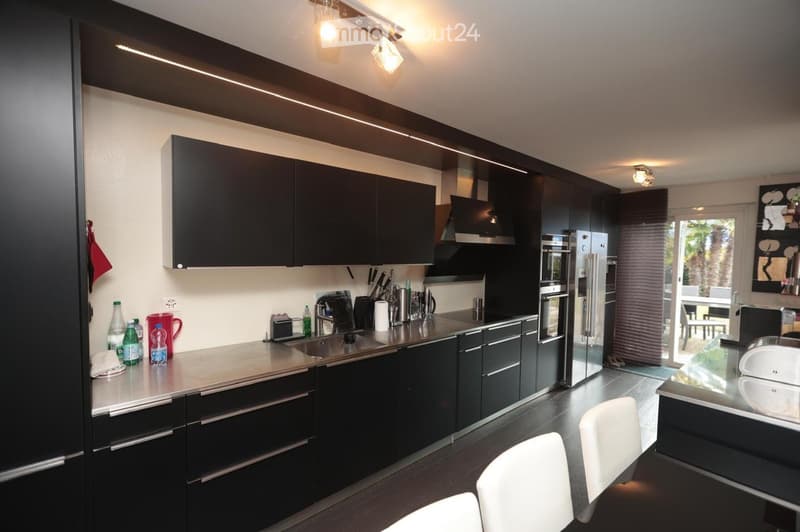 modern kitchen with black cabinets, stainless steel countertops, white chairs, and a glass door leading to a balcony