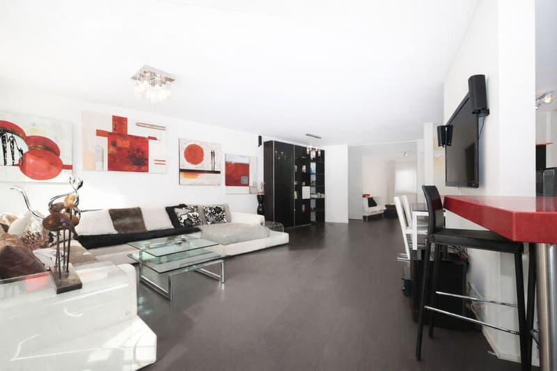 modern living room with white walls, dark wood floor, white sofa, glass coffee table, black bar stools, mounted TV, abstract paintings