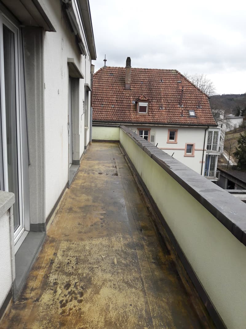 Balcony with concrete floor, white walls, and a view of a house with a red roof