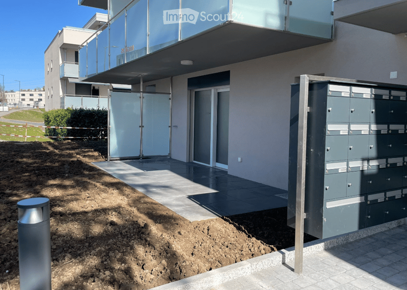 Modern building with glass balcony, raised ground floor, entrance with sliding glass doors, paved entrance, mailboxes