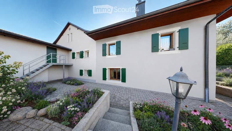 Two-story white house with green shutters, raised ground floor, garden, and steps leading to a balcony.