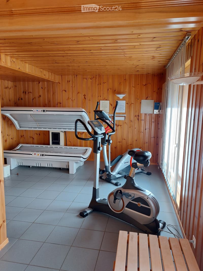 A room with wooden walls and tiled floor, containing a tanning bed, an exercise bike, and a recumbent bike.