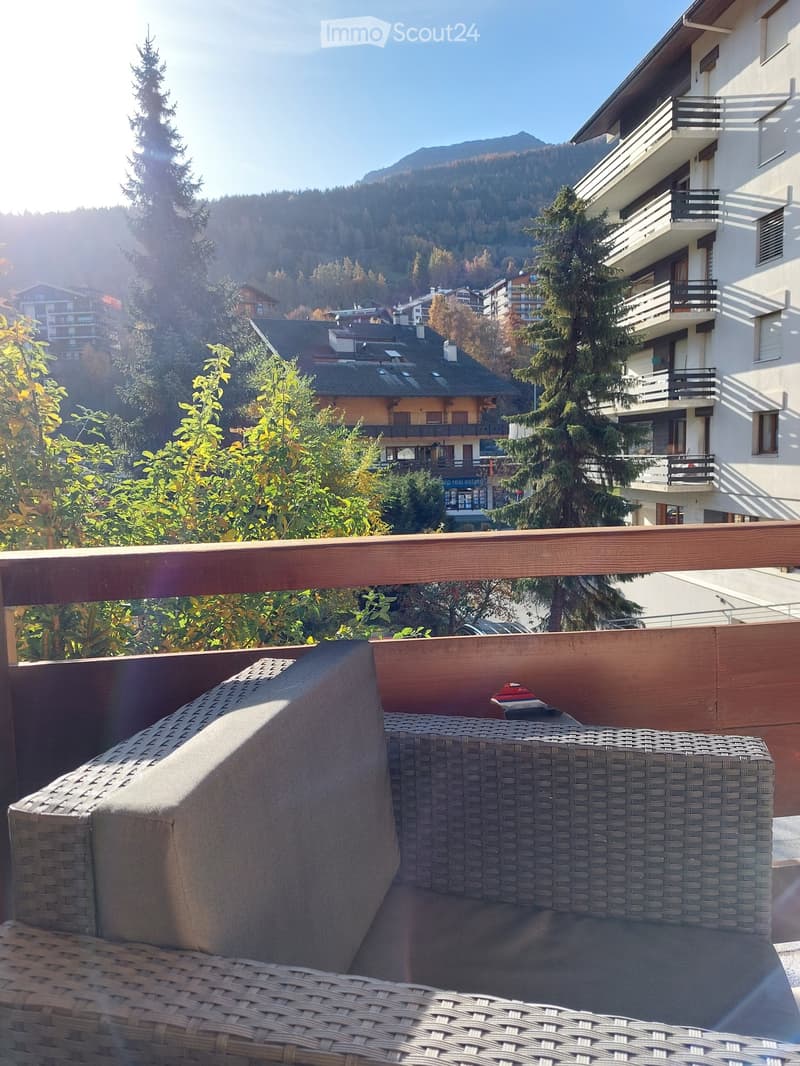 Balcony with wicker sofa, wooden railing, view of mountains and trees