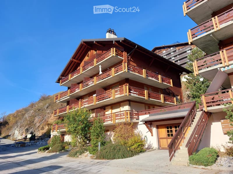 multi-story building, wooden balconies, brown wooden doors, white walls, mountain in the background