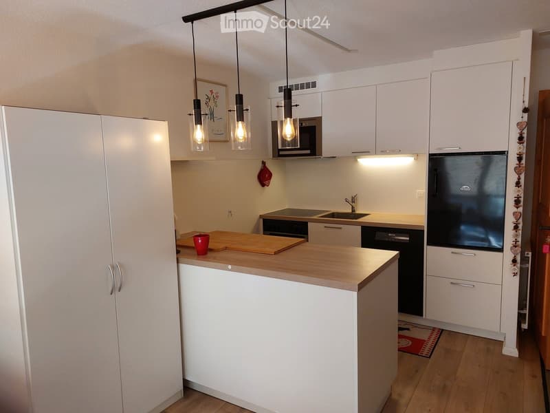 modern kitchen with white cabinets, wooden countertop, black appliances, pendant lights, wooden floor