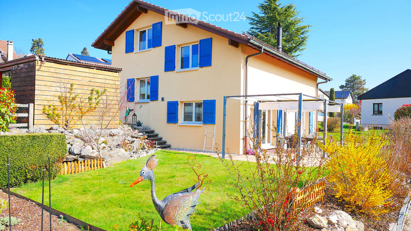House. 2 story house, yellow exterior, blue shutters, solar panels, garden, patio, lawn, decorative bird statue