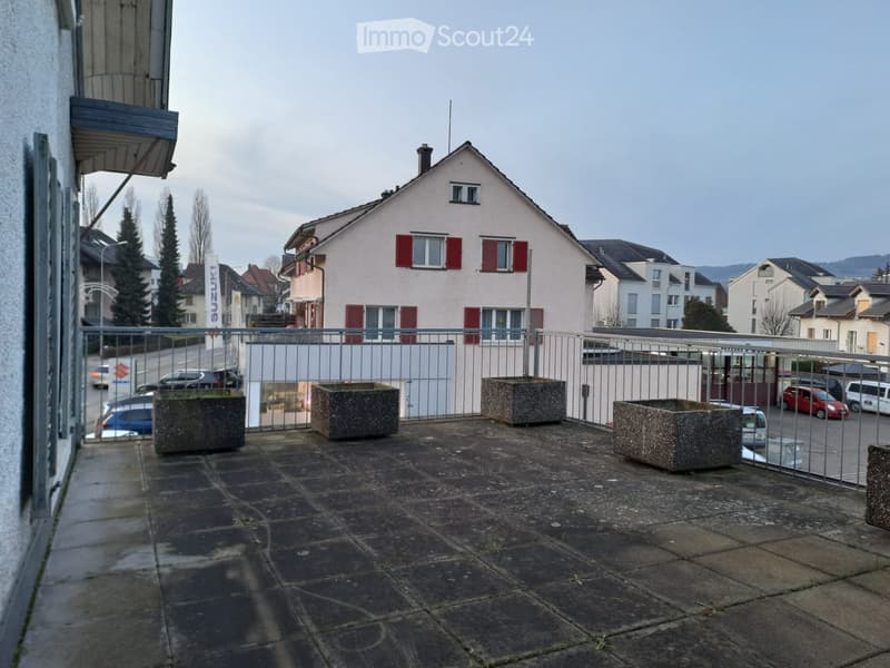 Balcony with metal railings, concrete floor, large concrete planters, view of street and houses