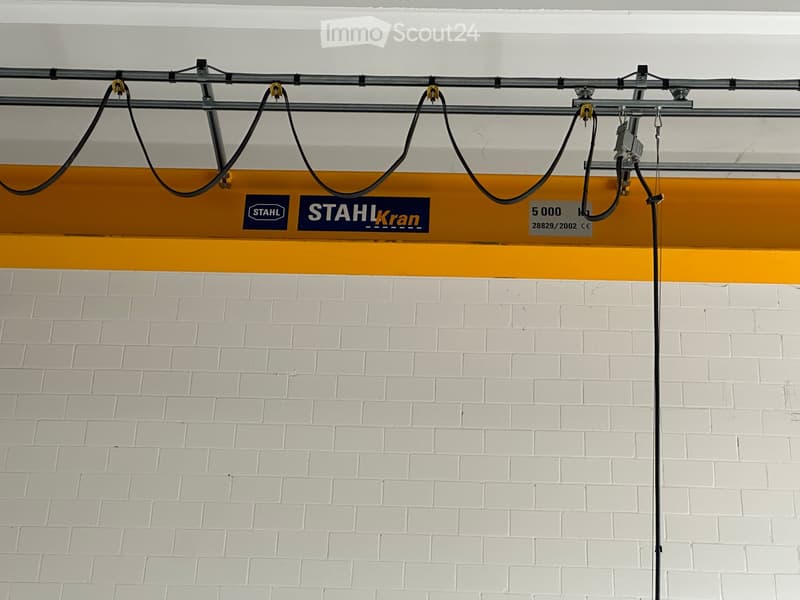 Industrial space with a yellow overhead crane, labeled 'STAHL Kran', capacity of 5000 kg, and a white brick wall.