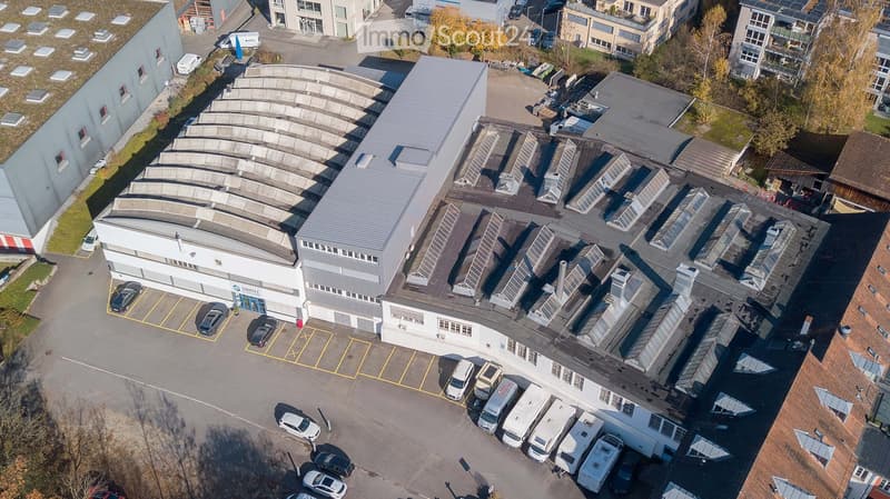 Large building with multiple floors, solar panels on the roof, multiple cars parked in front