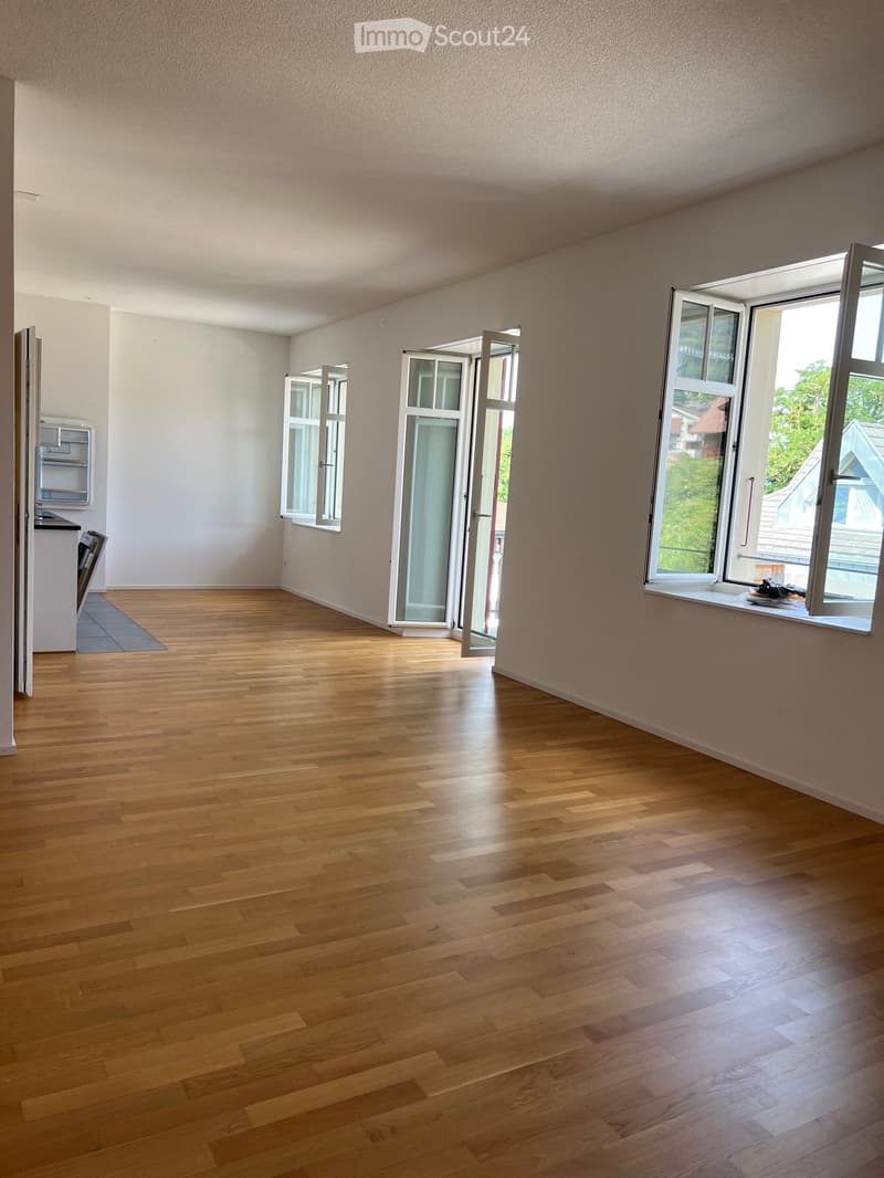 Empty room with wooden flooring, large windows, and open doors leading outside.