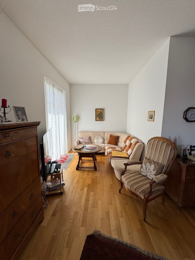 living room with wooden floor, beige sofa, wooden coffee table, wooden chair, wooden cabinet, TV, picture frames, clock, floor lamp