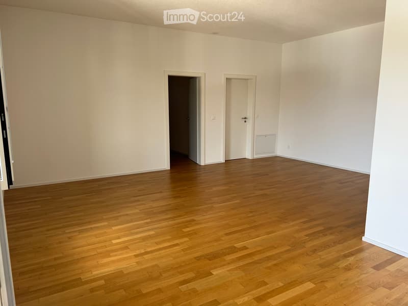 Empty room with light-colored walls and wooden flooring, featuring two doors and a radiator on one wall.