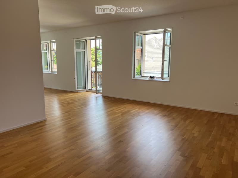 Empty room with wooden flooring, large windows, and sliding glass doors leading to a balcony.