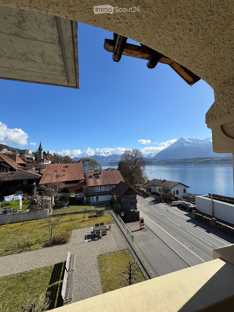 View from balcony of a village with houses, a road, a lake, and mountains in the background