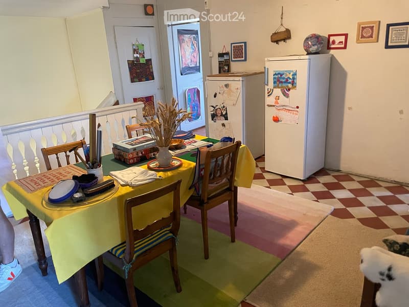 A cozy kitchen with a checkered floor, a yellow tablecloth on the dining table, and various items including a vase with dried plants, a bowl, and picture frames on the walls.