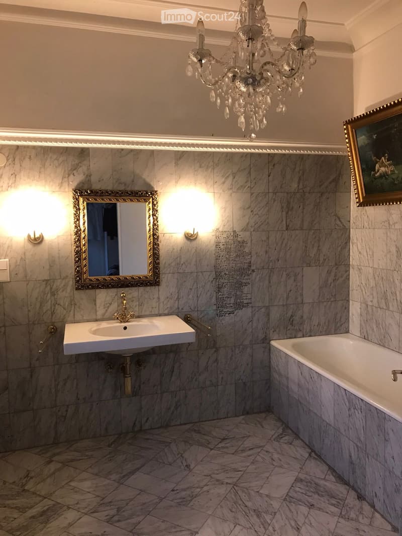 Bathroom with marble tiles, white bathtub, white sink, gold mirror, chandelier, wall-mounted lights