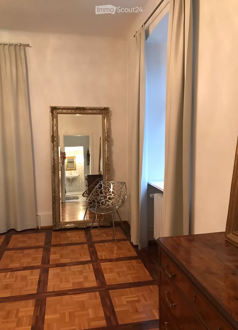 large mirror, wooden parquet floor, white walls, white curtains, silver chair, wooden dresser