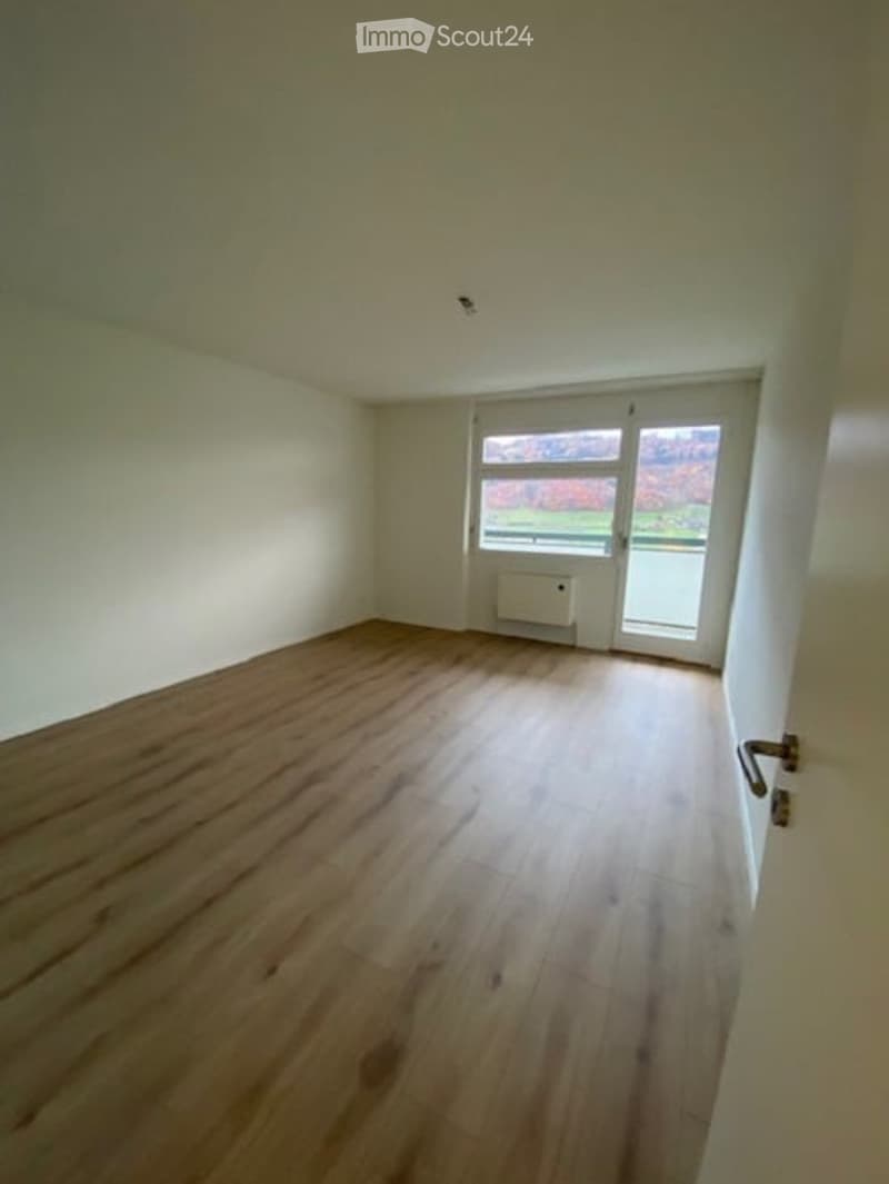 Empty room with wooden floor, white walls, glass door, and window