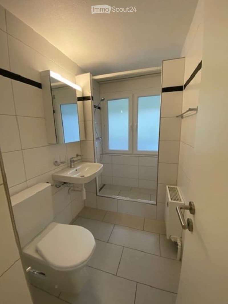 Bathroom with white tiles, toilet, sink, shower, mirror, and radiator