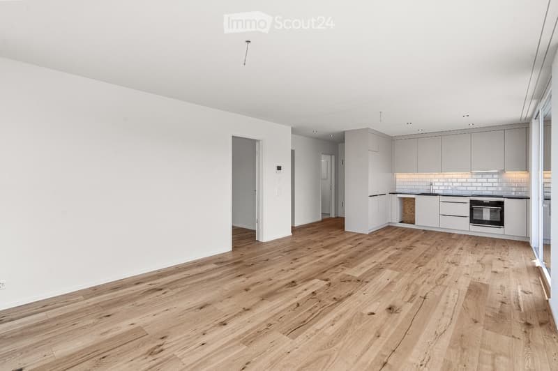 Modern kitchen with light grey cabinets, a central island, and a wooden floor. The space includes a sink, oven, and ample storage.
