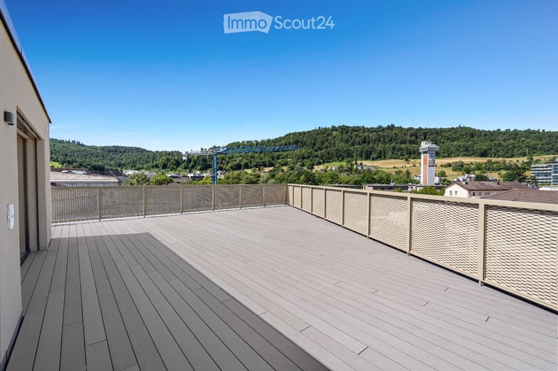 A modern wooden deck terrace with a metal railing, overlooking a scenic landscape with trees and a distant cityscape.