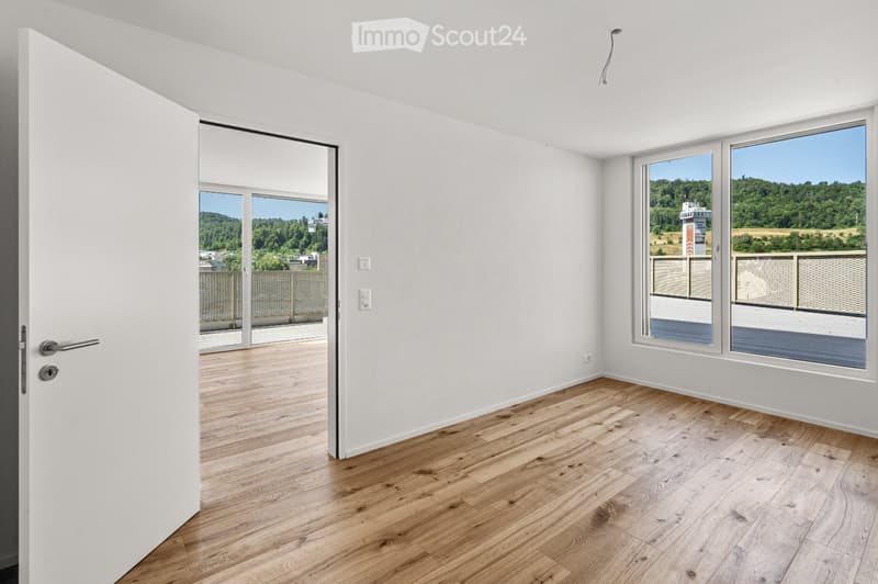 Empty room with light wooden flooring, white walls, large windows offering a scenic view, and a sliding door leading to a balcony.
