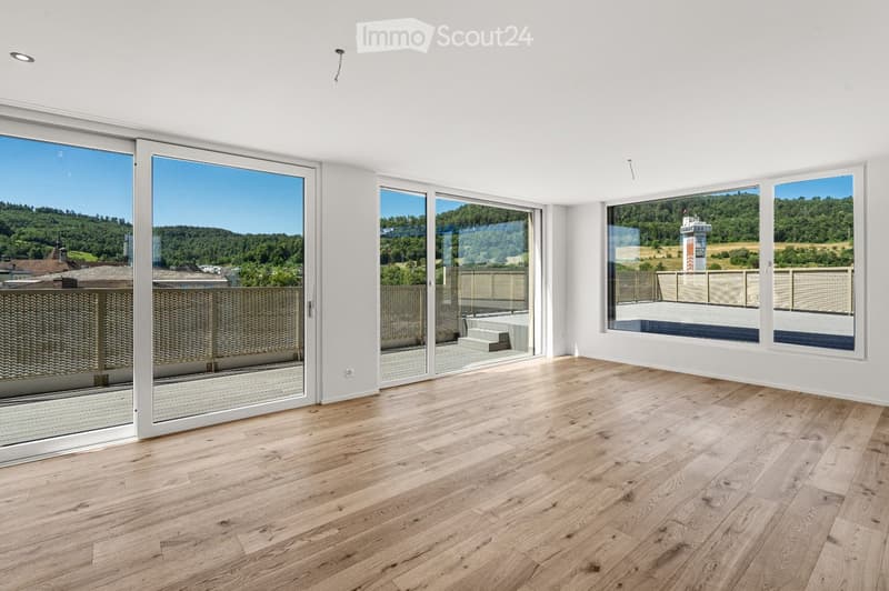 Empty room with wooden flooring, large windows, and sliding glass doors leading to a balcony with scenic views.