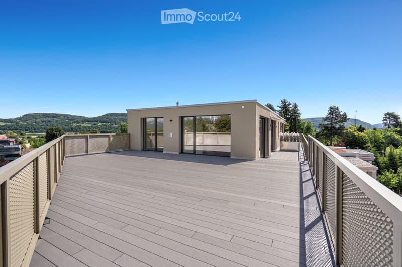 Modern rooftop terrace with wooden decking, metal railings, and panoramic views of a green landscape and hills.