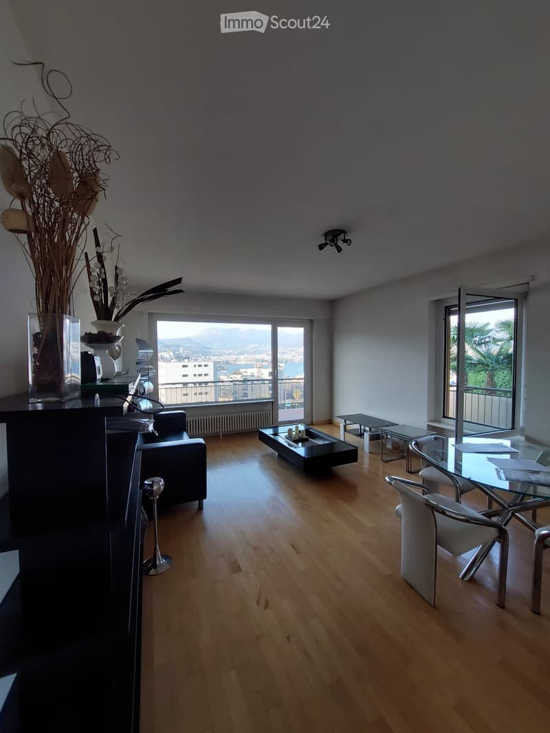 modern living room with wooden floor, large windows, glass table, black couch, white chairs, decorative vase, balcony