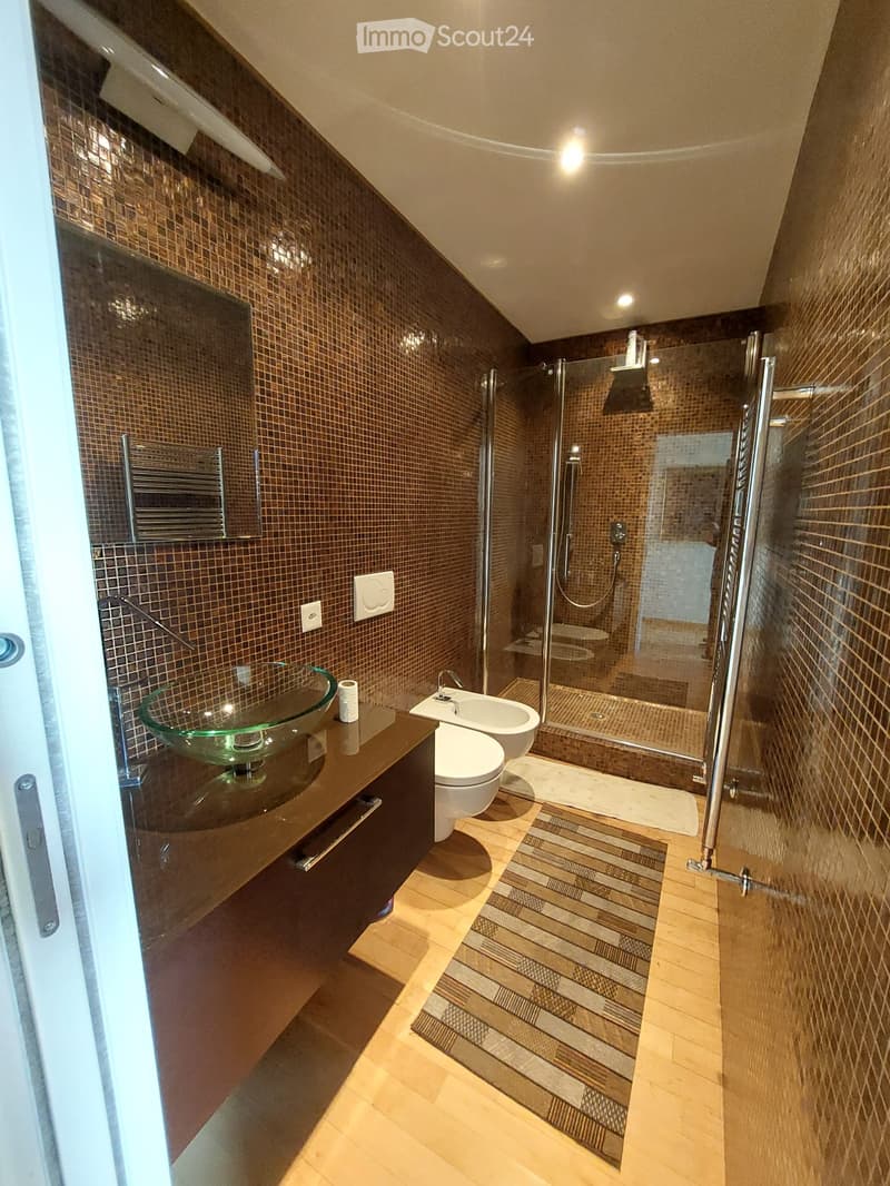 modern bathroom with brown tiles, glass sink, white toilet, glass shower enclosure, wooden floor