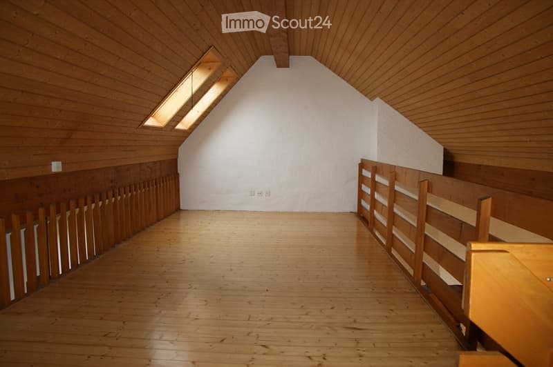 Wooden attic space with slanted ceiling, wooden floor, and wooden paneled walls. The room has a loft-like feel with a simple, minimalist design.