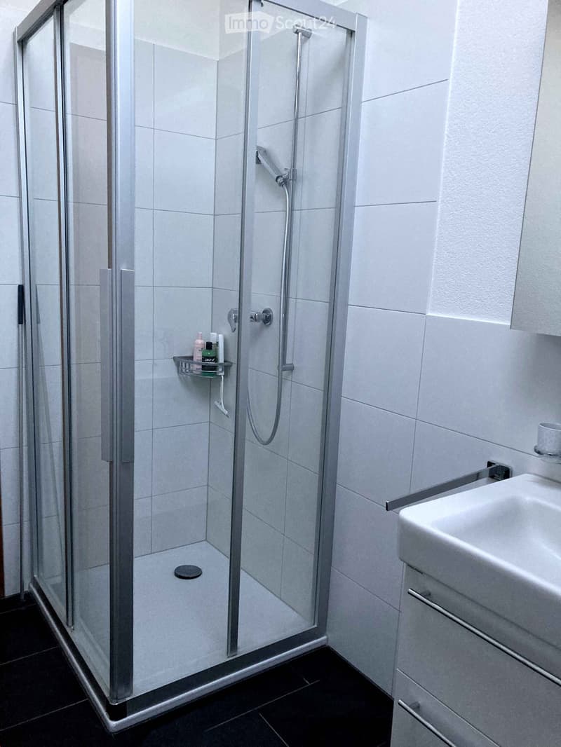 Tiled bathroom with glass shower enclosure, vanity unit, and a washing machine.