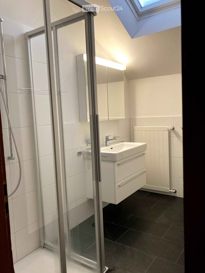 Bathroom with glass shower enclosure, white vanity with sink, and tiled floor.