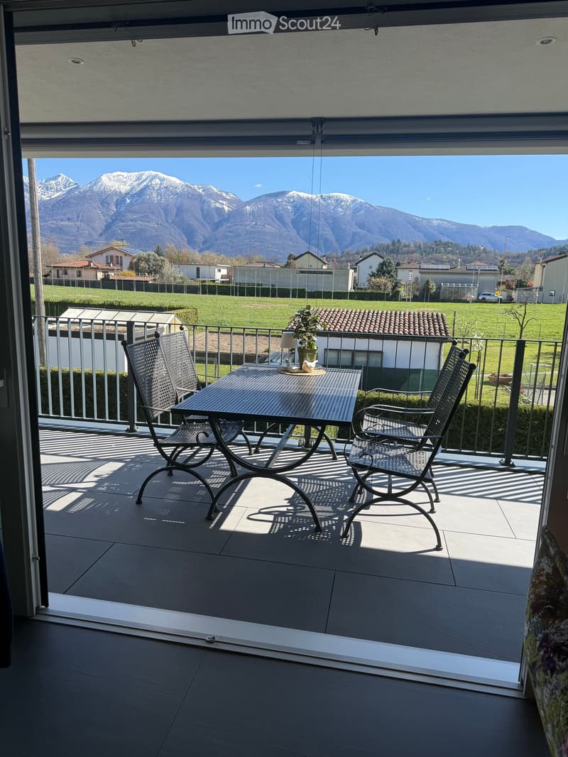 Balcony with table and chairs, metal railing, tiled floor, view of mountains and houses