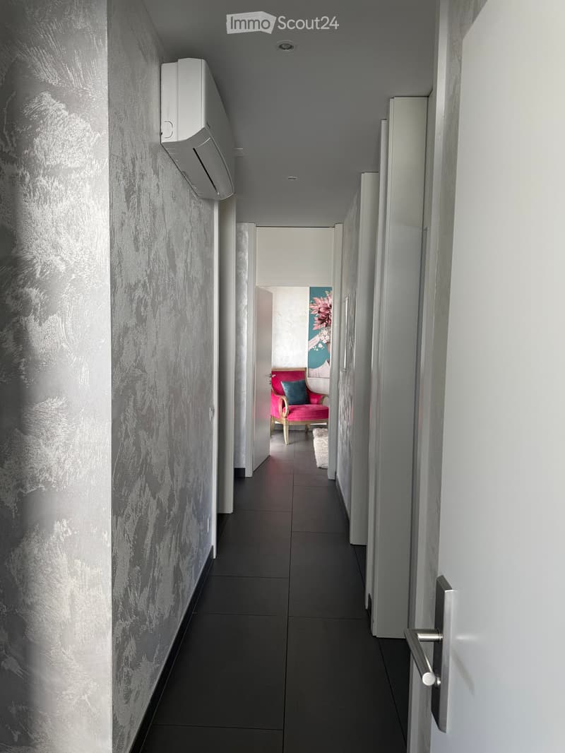 Corridor with silver wallpaper, black tiles, air conditioner, open door to living room with pink chair and white rug