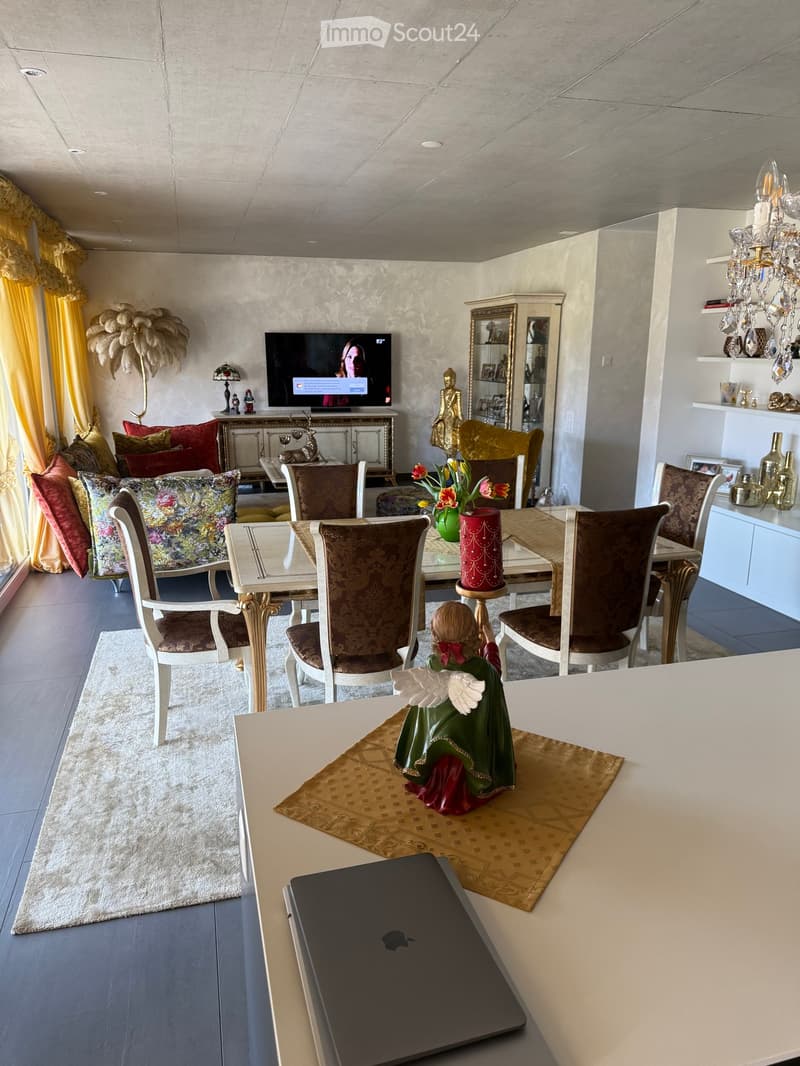 Dining room with a table, chairs, a TV, a rug, a chandelier, a statue, a lamp, a cabinet, a couch, and pillows