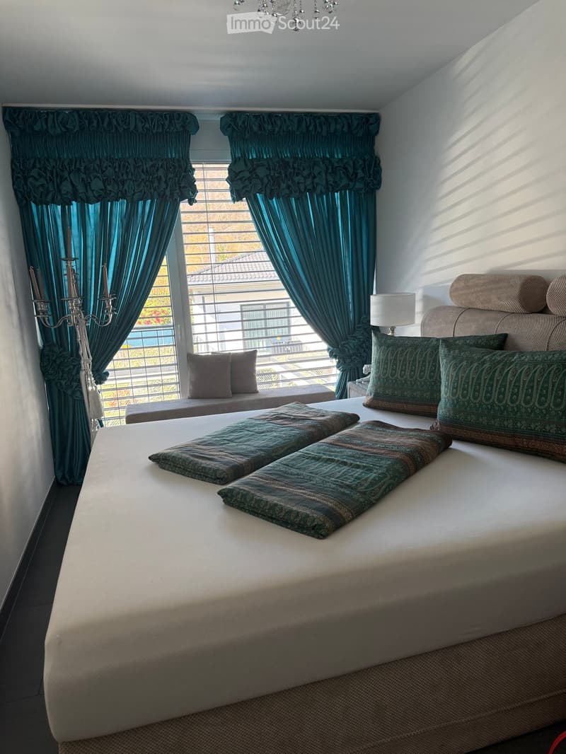 large bed, white sheets, green pillows, white lamp, blue curtains, window seat, chandelier
