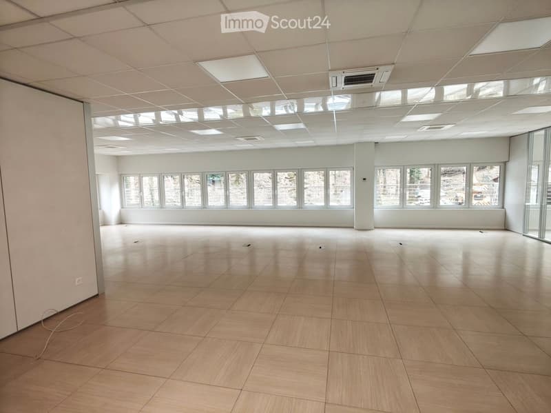 Empty room with white walls, wooden floor, large windows, ceiling with lights and air conditioning units